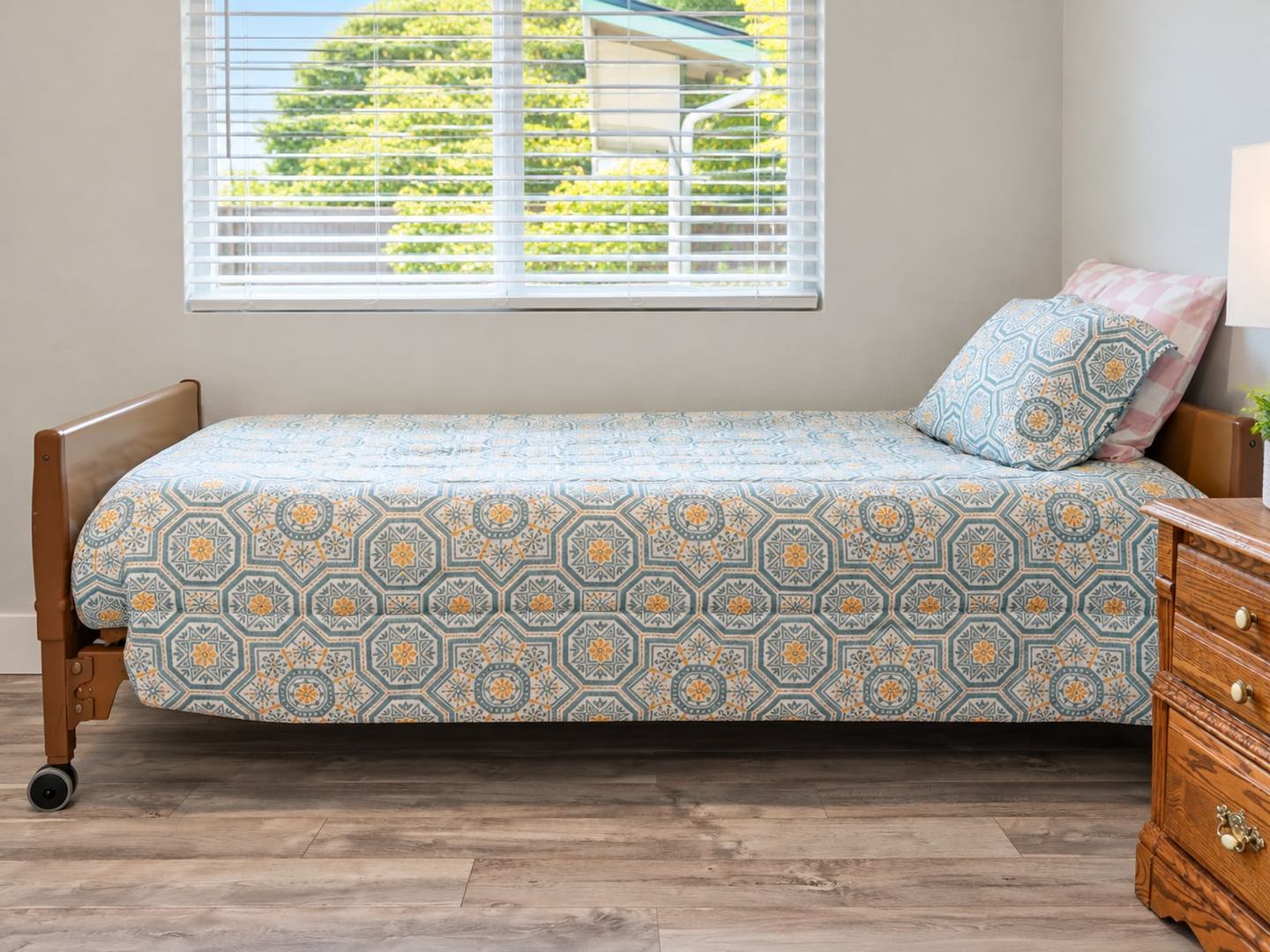 Single bed with a patterned quilt beneath a sunny window